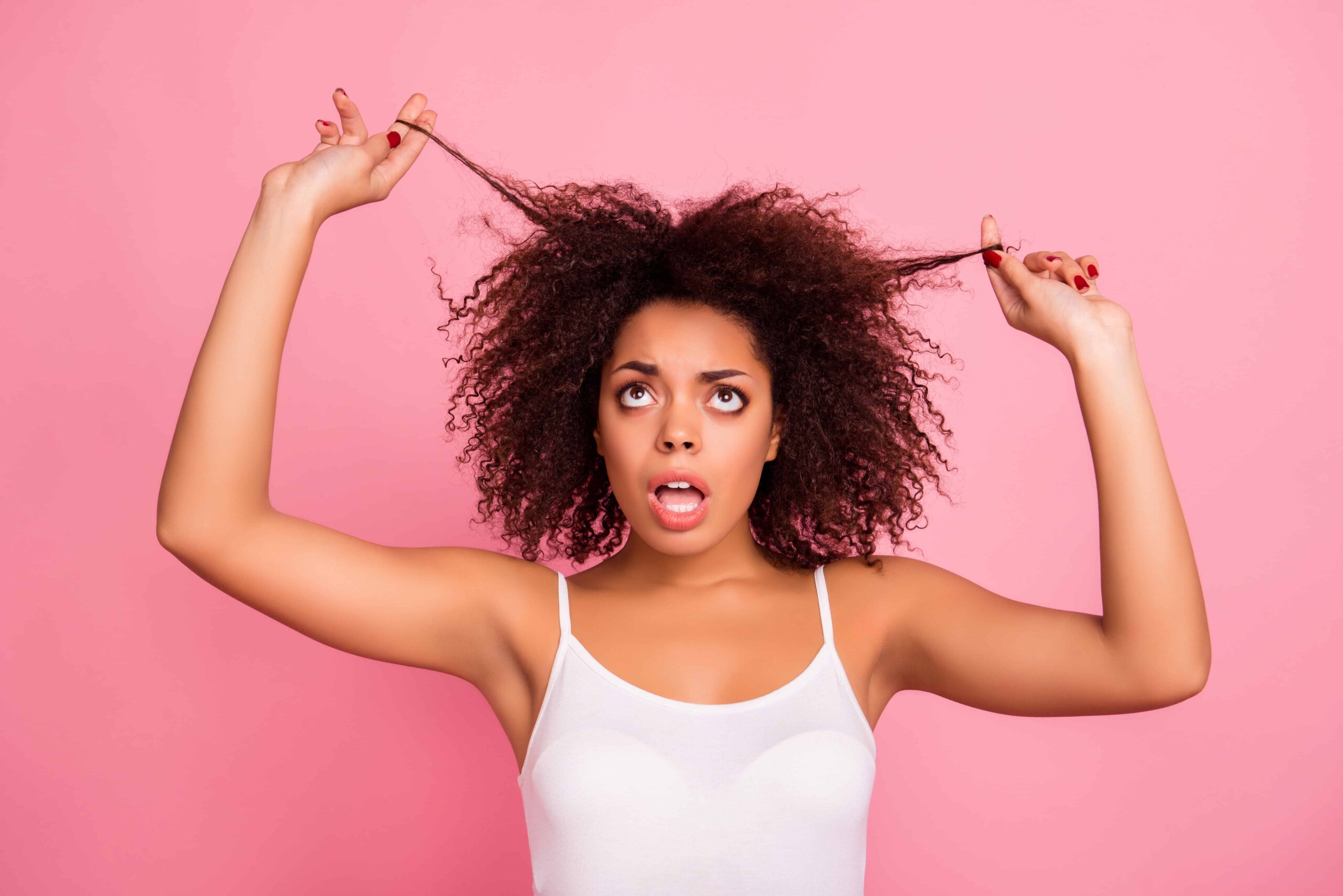 Curly haired woman tugging at her hair on pink background.