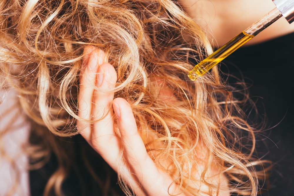 Close up of curly haired girl applying oil to curly hair.