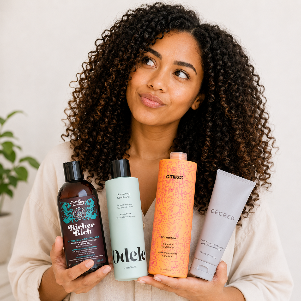 Woman with curly hair holding four conditioners recommended for low porosity hair, including Odele, Amika Normcore, CÉCRED Moisturizing Conditioner, and Uncle Funky’s Daughter Richer Rich, while looking thoughtfully upward against a neutral background
