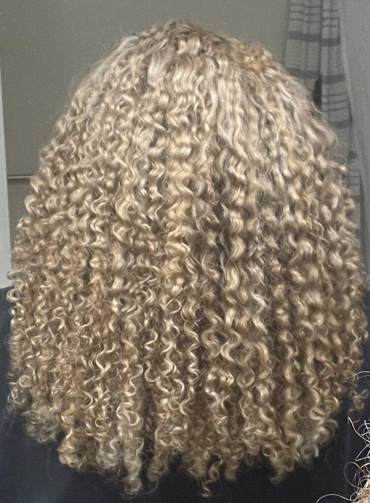 Back view of Author's fully blonde, bleached curls, defined and clumped, an example of a rougher, more permeable cuticle.