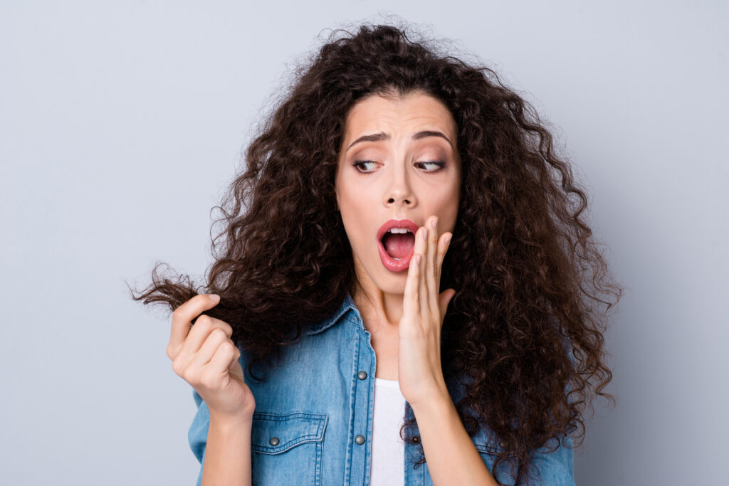 Image of Curly Haired woman looking at the ends of her hair. Are Silicones in Hair Products Always Bad?