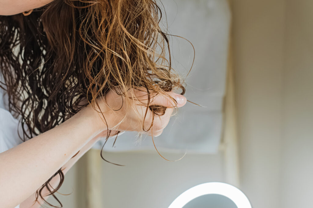 Wavy haired woman scrunching product into her hair. Best Mousse for Curly Hair plus Key Ingredients.