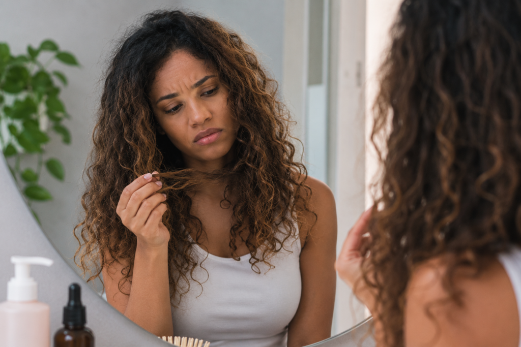 Woman with partially recovering curls showing uneven curl definition and texture, representing the gradual recovery process of heat-damaged curly hair over time.